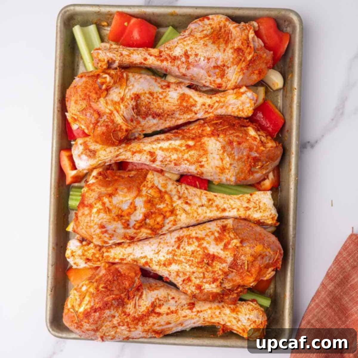 Seasoned, raw turkey legs and vegetables on a baking tray before cooking.