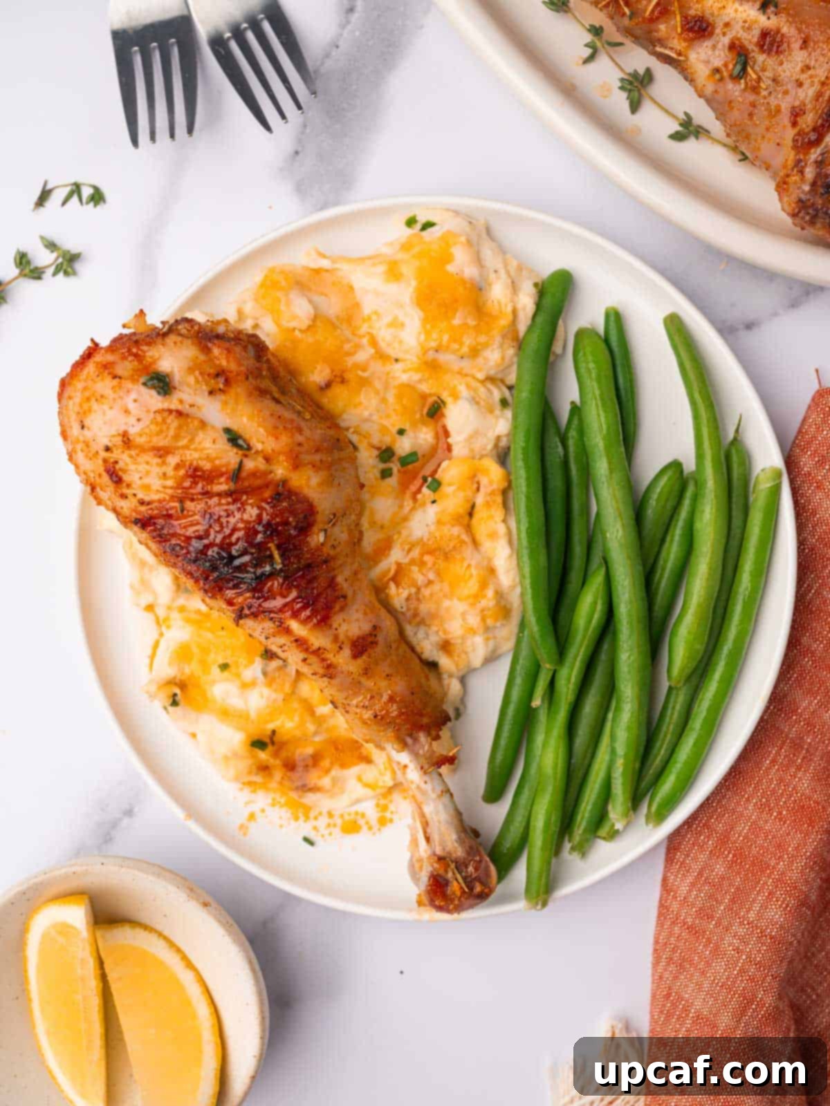 A baked turkey drumstick on a plate with cheesy mashed potatoes and green beans.