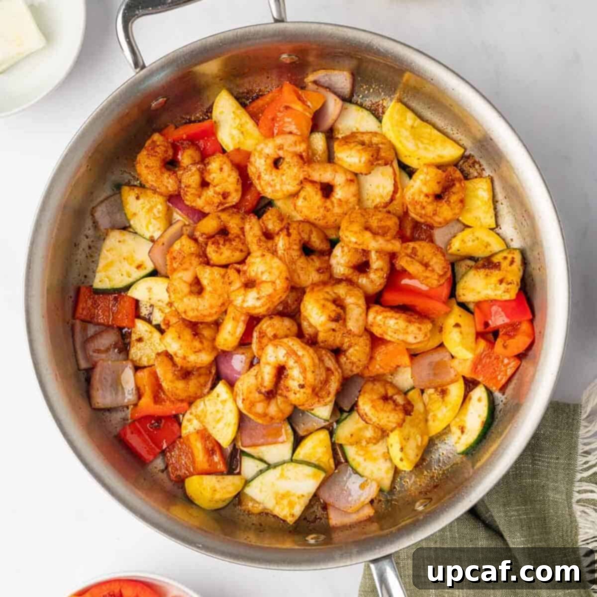 Sauteed shrimp added ove sauteed vegetables in a skillet.