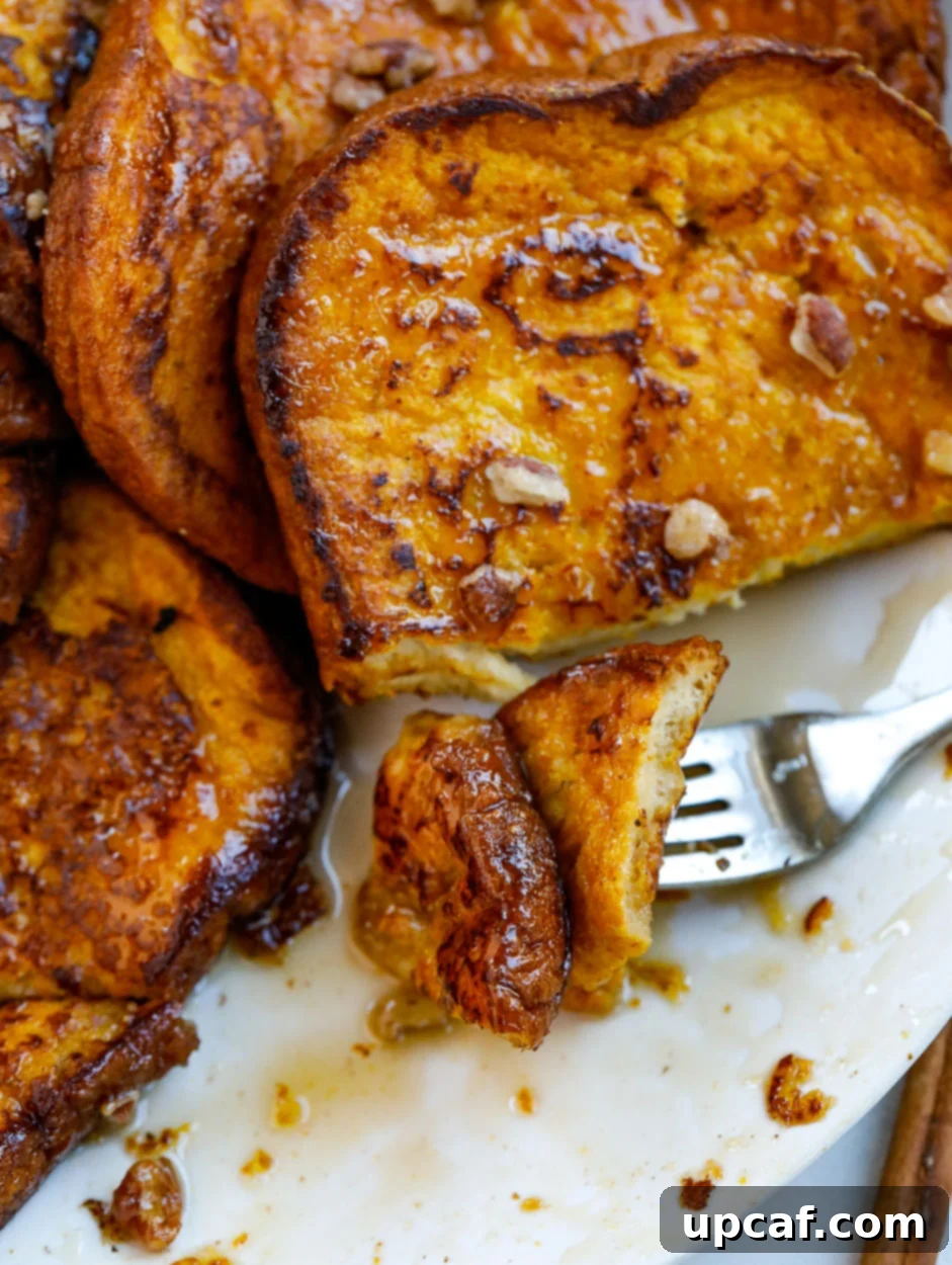 Close-up of a perfectly cooked pumpkin French toast slice on a fork, ready to be enjoyed.