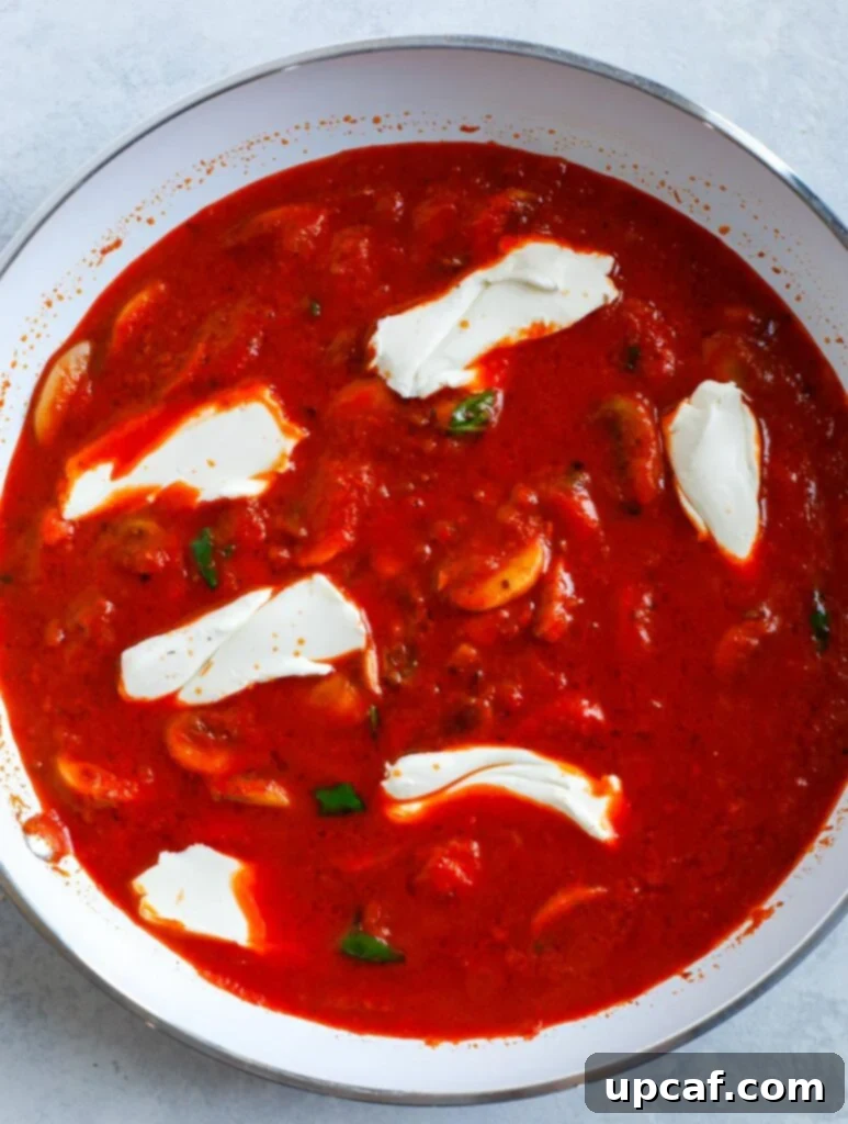 Cream cheese melting into the rich red pepper sauce in a skillet, creating a luscious texture