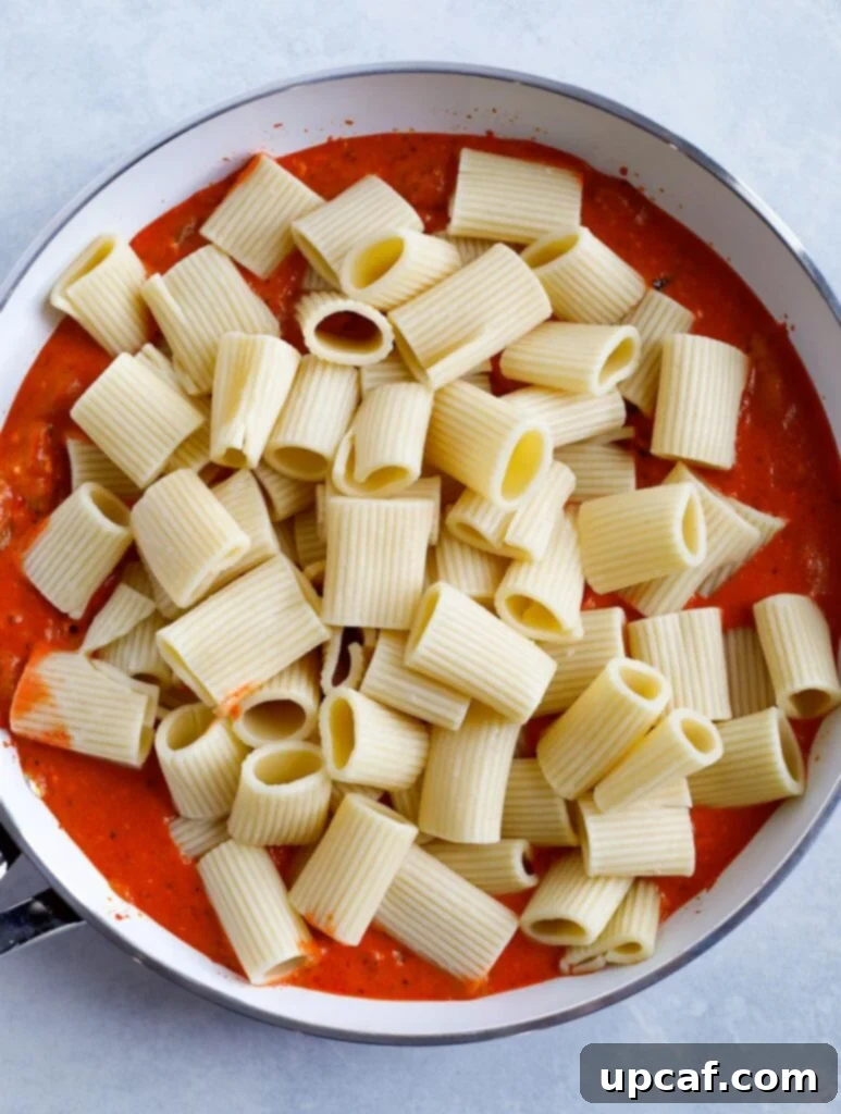 Cooked rigatoni pasta being tossed in the creamy red pepper sauce, ensuring every piece is coated