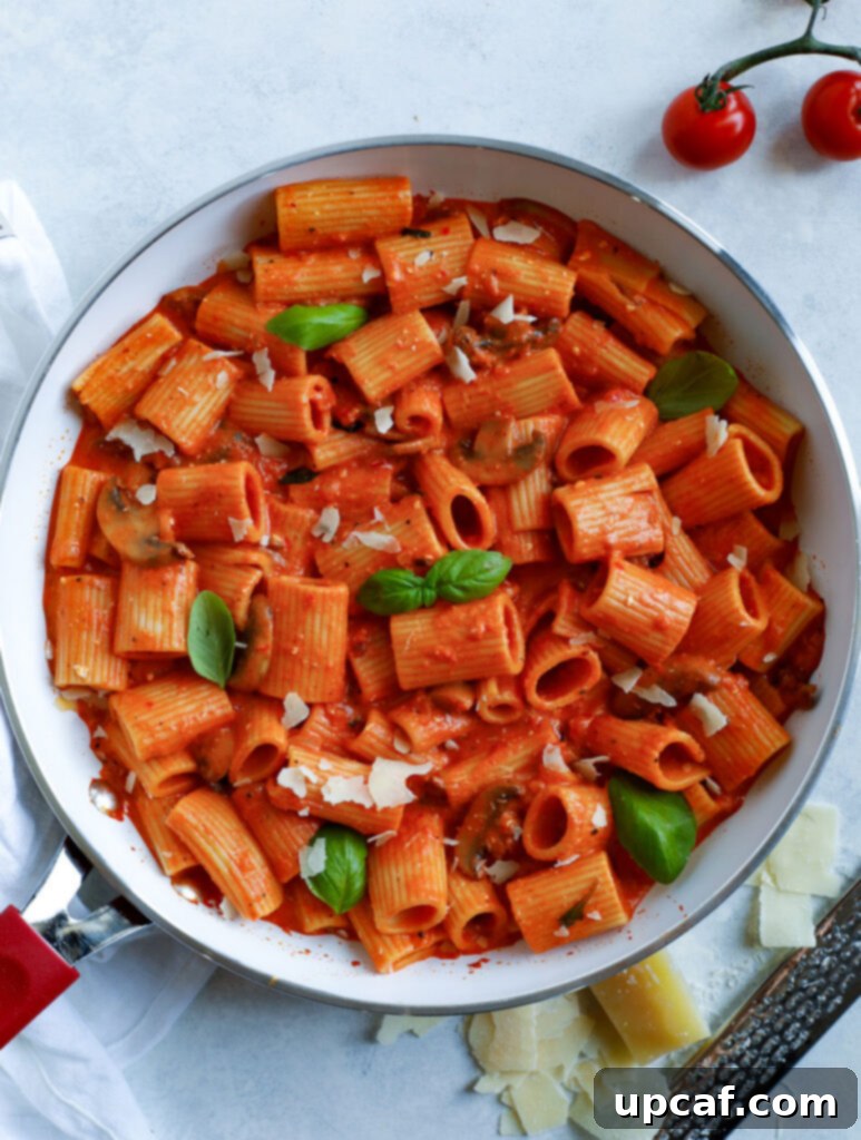 Top-down view of Creamy Red Pepper Rigatoni Pasta in a bowl, garnished with fresh basil and Parmesan