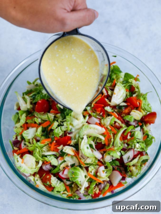 Creamy lemon-mayo dressing being poured over a bowl of fresh, chopped vegetables for the salad.