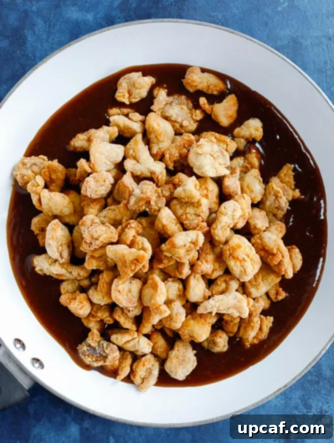 fried chicken bites over the orange chicken sauce in a white skillet before mixing.