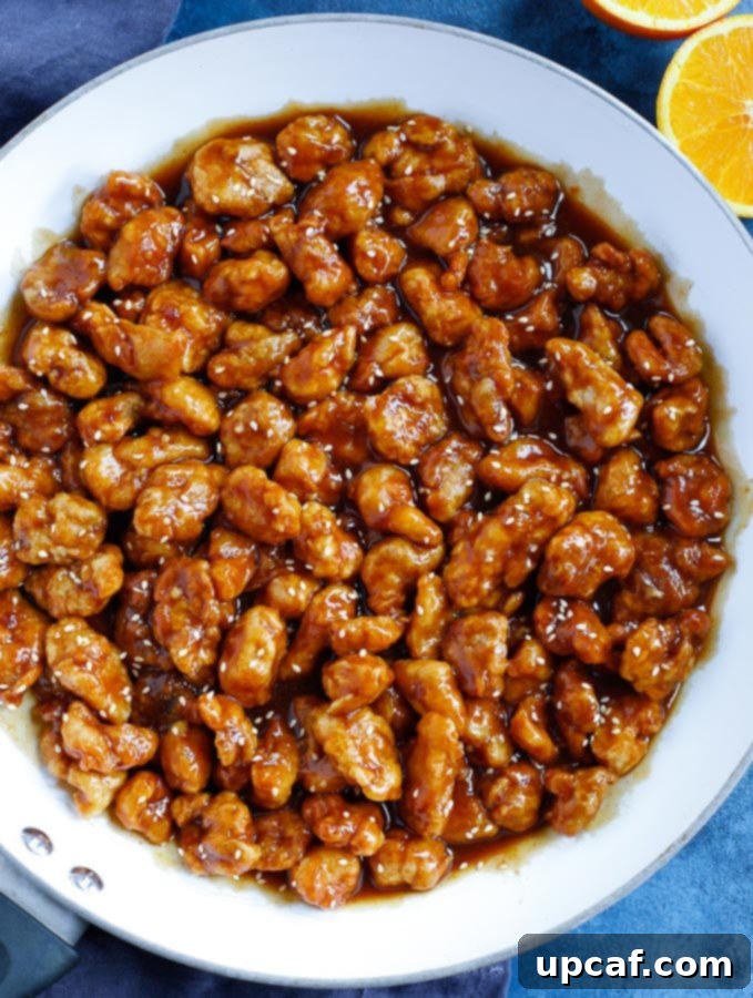 fried chicken bites over the orange chicken sauce in a white skillet after mixing with the sauce.