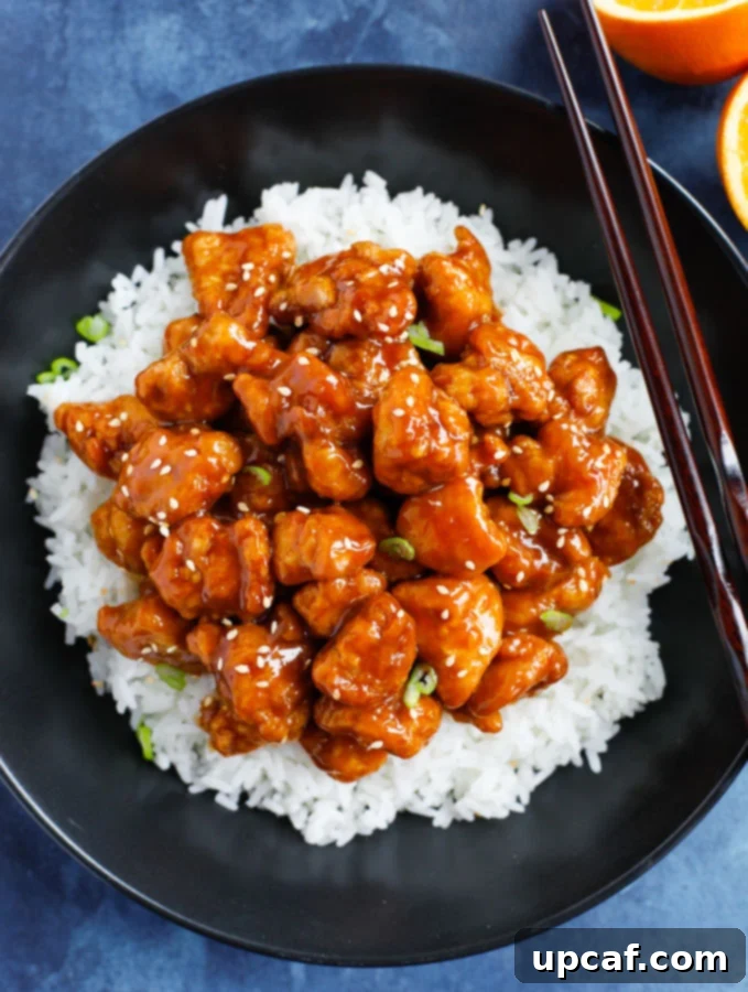 Orange chicken recipe served on a bed of white rice with chops sticks on the side.