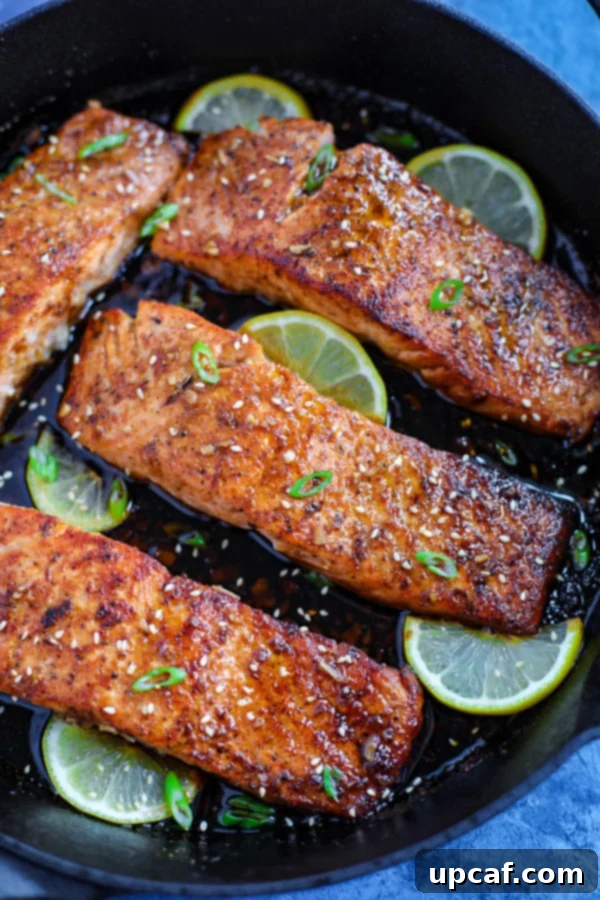 Four perfectly cooked spicy honey garlic salmon fillets, garnished with fresh lime wedges, served in a rustic cast iron skillet.