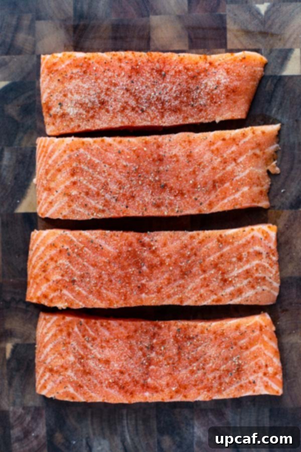 Four raw, unseasoned salmon fillets resting on a clean cutting board, ready for preparation.