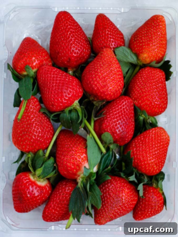 A vibrant collection of fresh, red strawberries neatly arranged in a clear container, ready for dipping.