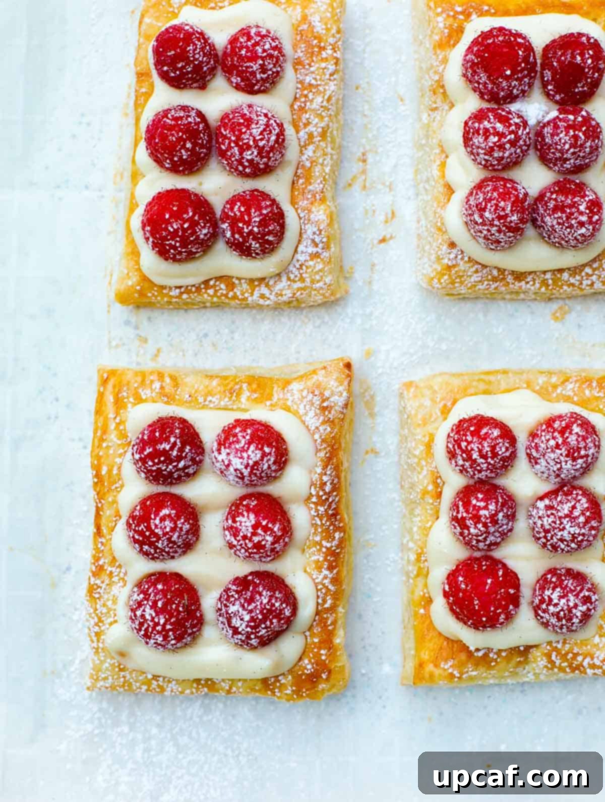 A sheet pan adorned with an array of baked raspberry tarts, each exquisitely dusted with powdered sugar, creating an inviting presentation.