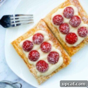 A beautifully arranged raspberry tart on a pristine white plate, delicately dusted with powdered sugar, ready to be enjoyed.