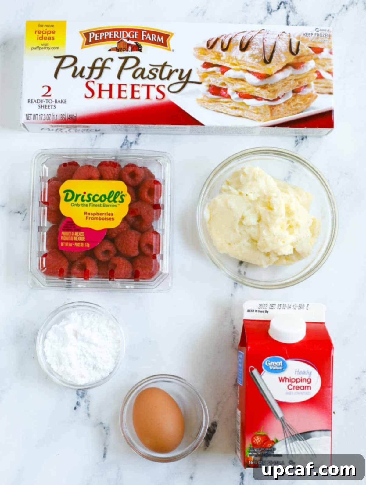 A vibrant flat lay image showcasing all the fresh ingredients needed to make delicious raspberry puff pastry tarts, including puff pastry sheets, fresh raspberries, eggs, and confectioners sugar.