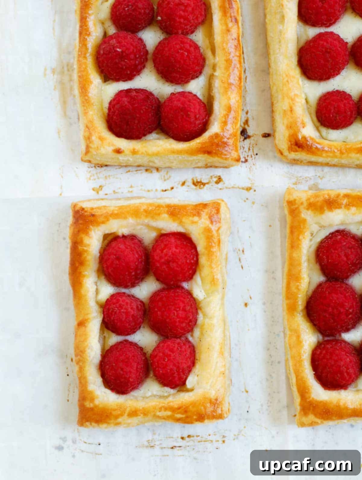 A baking sheet filled with freshly baked raspberry tarts, golden and inviting, just out of the oven.