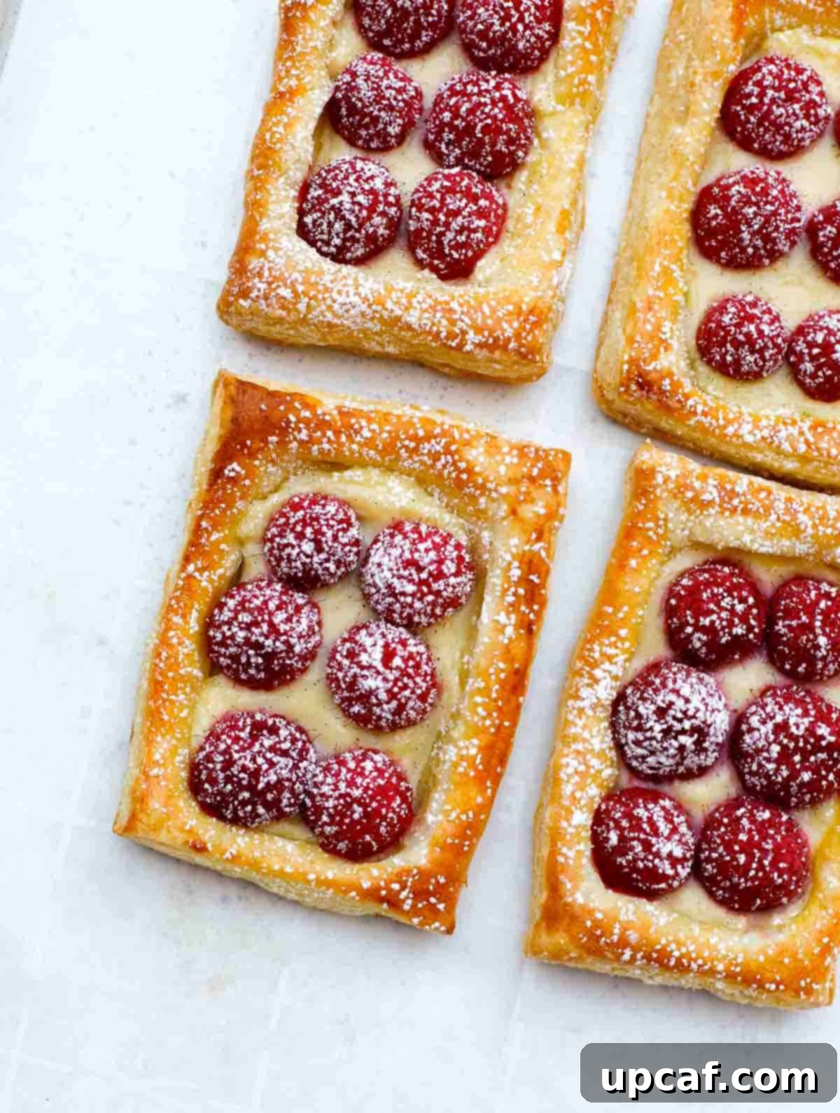Freshly baked raspberry tarts on a baking sheet, delicately dusted with a snowy layer of powdered sugar, making them irresistible.