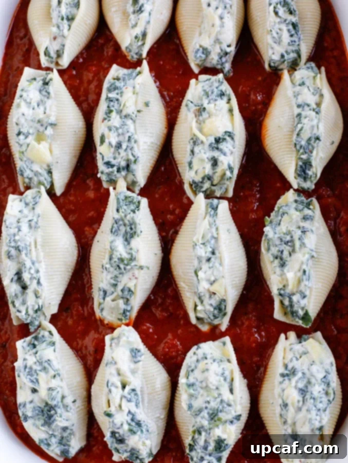 Spinach artichoke stuffed shells lined up in a baking dish, ready for sauce and cheese.