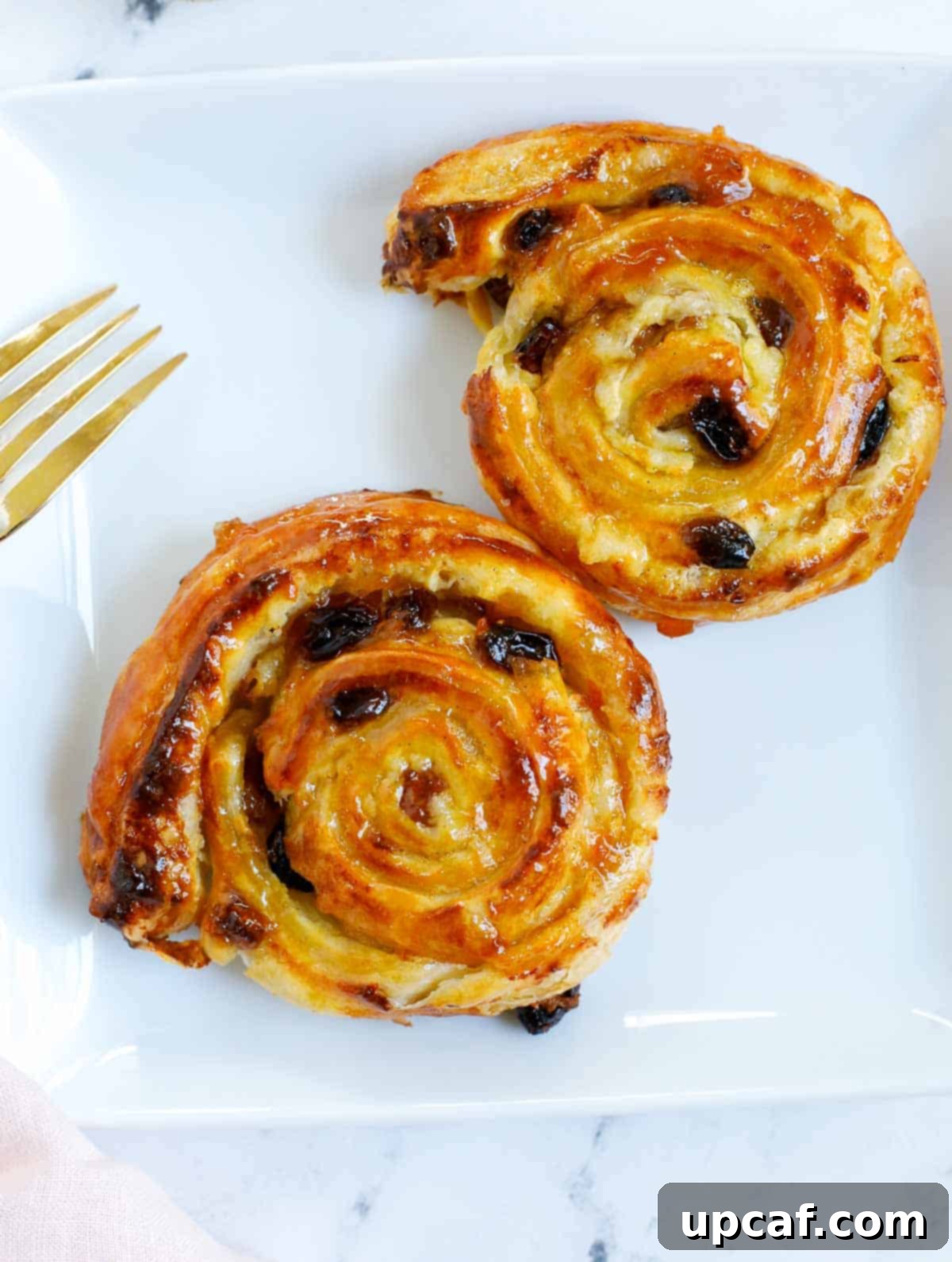 Effortless Pain Aux Raisins 14 two baked pain aux raisins on a white plate.