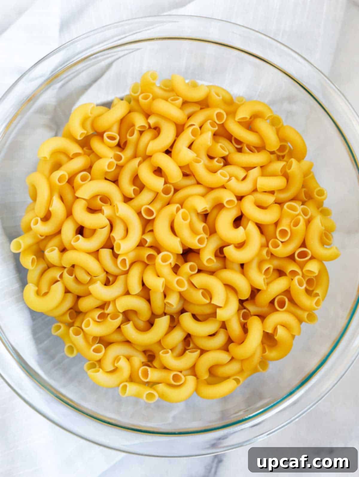 Golden Baked Creamy Mac & Cheese 2 Raw elbow macaroni noodles in a bowl, surrounded by blocks of cheese, milk, butter, and various spices, ready for making mac and cheese.