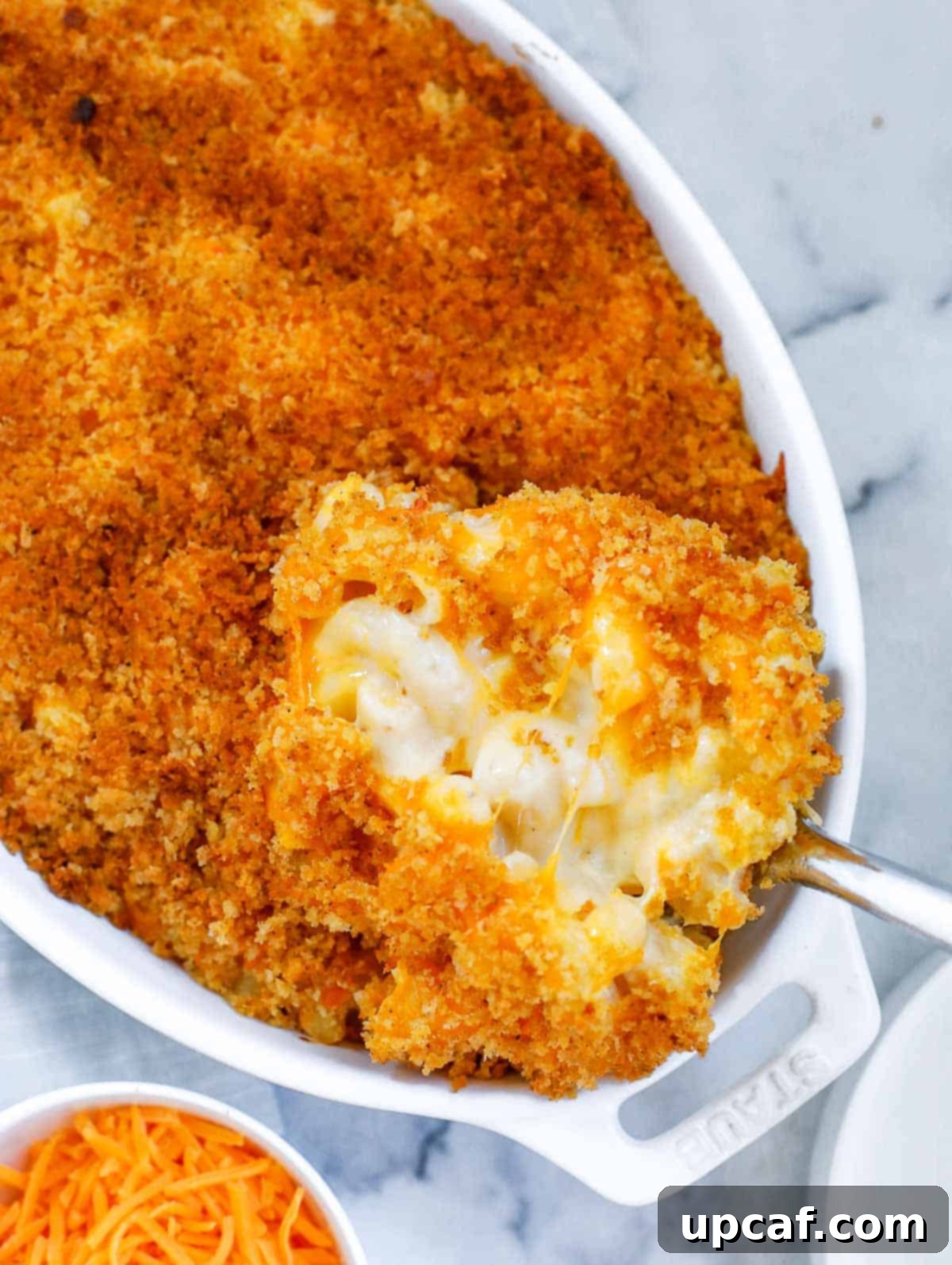 Golden Baked Creamy Mac & Cheese 5 A serving spoon lifting a portion of hot, creamy baked mac and cheese from a baking dish, showcasing its cheesy interior and crispy top.