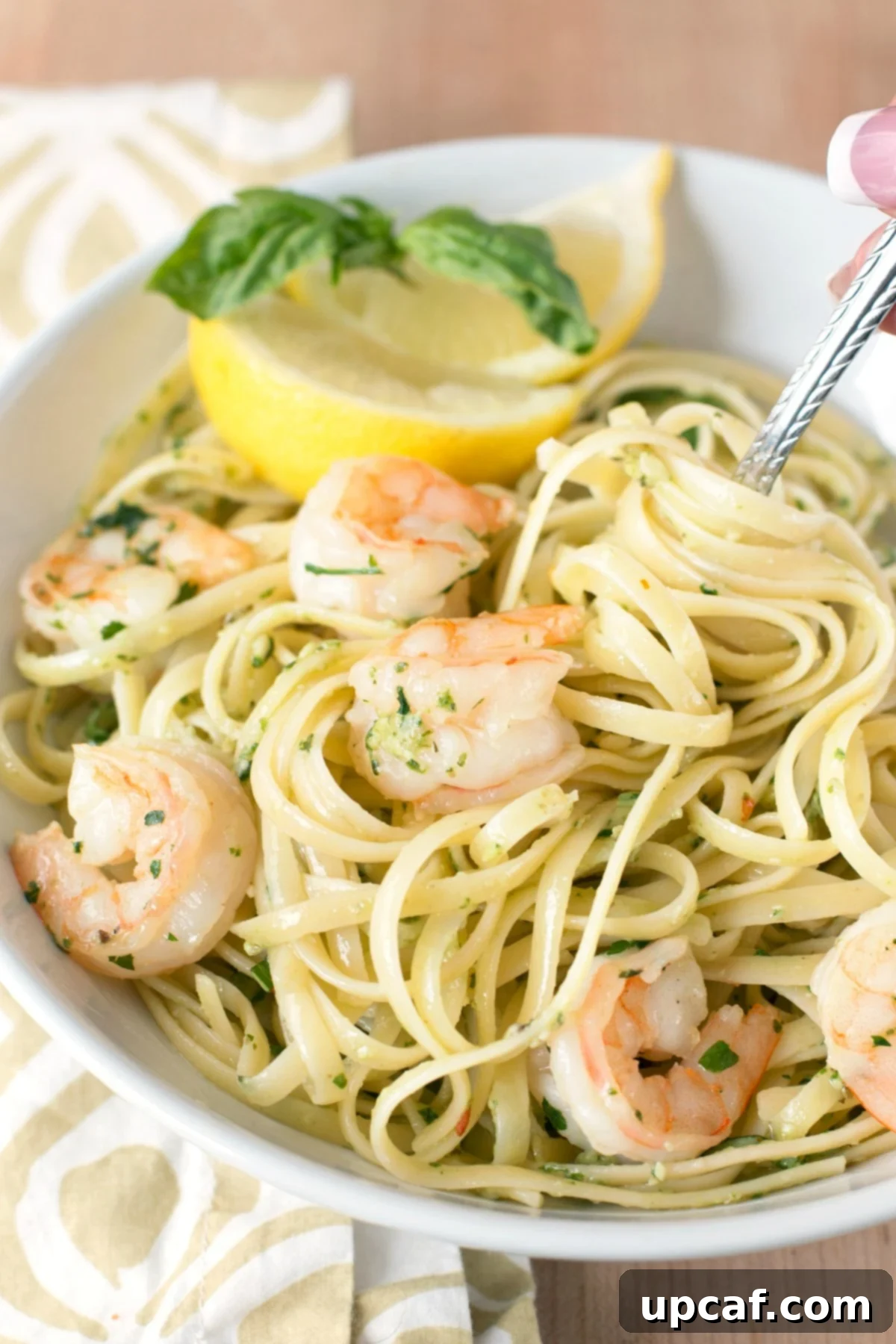 Overhead picture of a large white bowl of pasta with pesto shrimp scampi and lemon slices