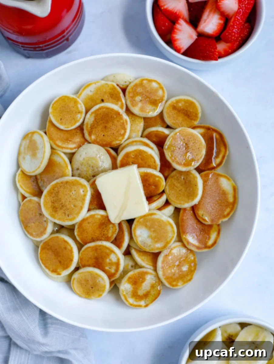 A bowl of delightful mini pancake cereal, generously topped with melted butter and sweet syrup, garnished with fresh banana slices and vibrant strawberries. This perfect breakfast spread promises a joyful start to any day.