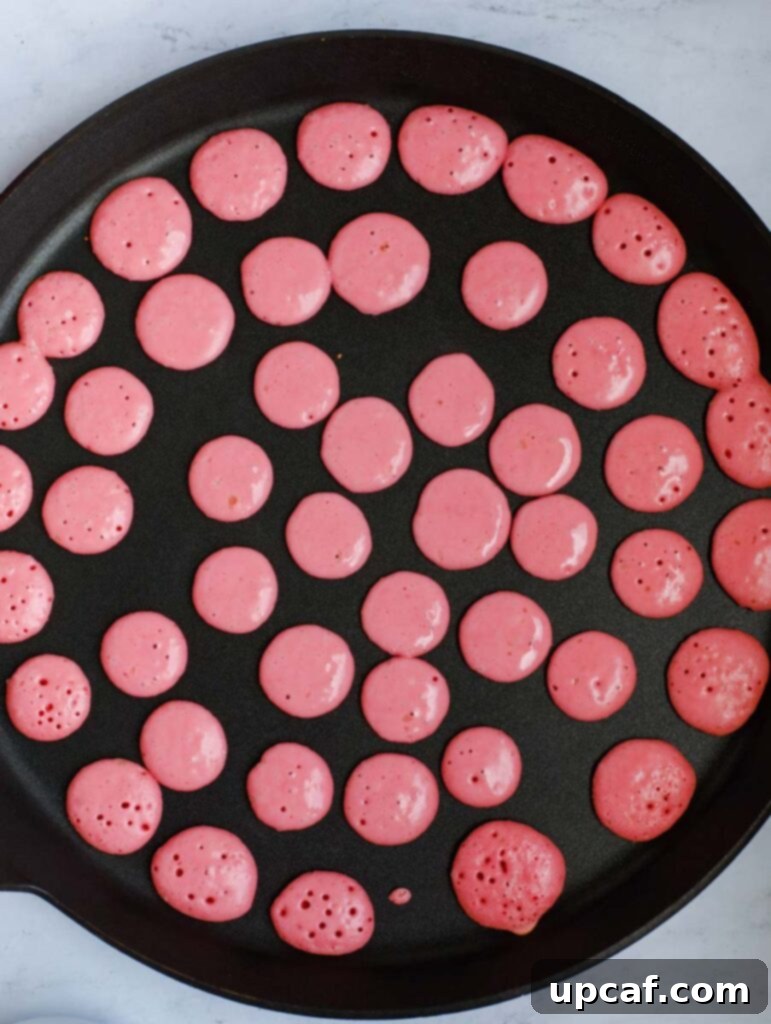 A batch of cheerful mini strawberry pancakes cooking on a hot griddle, showcasing their charming pink color and perfect tiny round shapes.