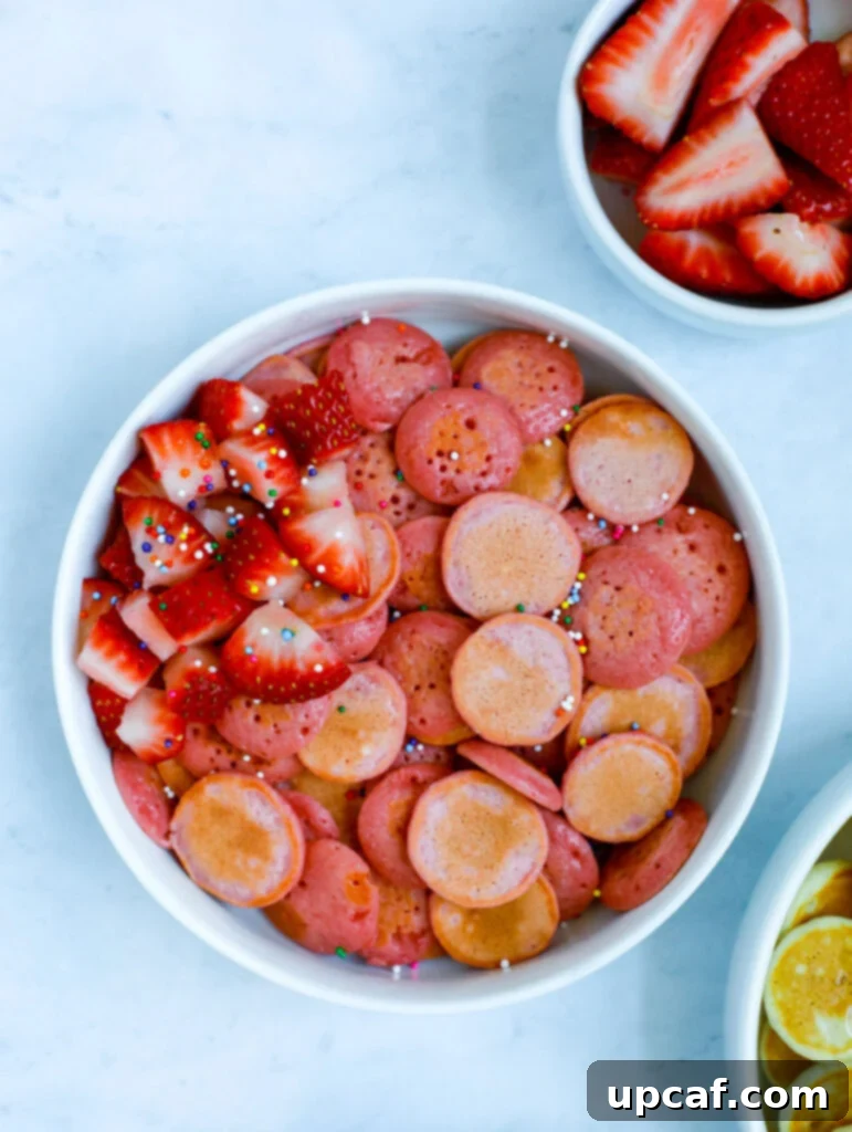 A delightful bowl of mini strawberry pancakes, brightly adorned with fresh strawberry slices and a festive shower of colorful sprinkles, ready to be enjoyed.