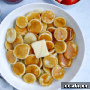 A bowl of delightful mini pancake cereal, generously topped with melted butter and sweet syrup, garnished with fresh banana slices and vibrant strawberries. This perfect breakfast spread promises a joyful start to any day.