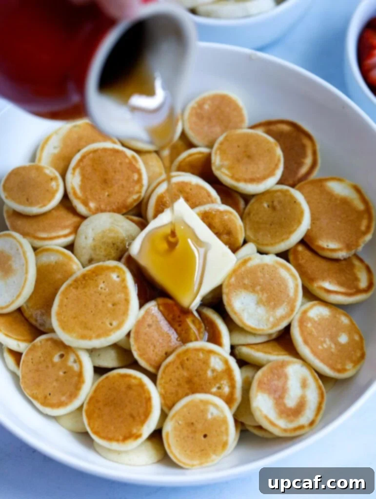 A mouthwatering image of a stack of freshly cooked mini pancakes, with a stream of golden pancake syrup being generously poured over them.