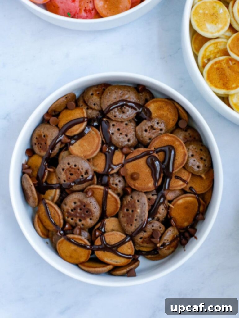 A charming bowl of mini chocolate pancake cereal, generously topped with luscious chocolate syrup and a scattering of sweet chocolate chips, creating an irresistible treat.