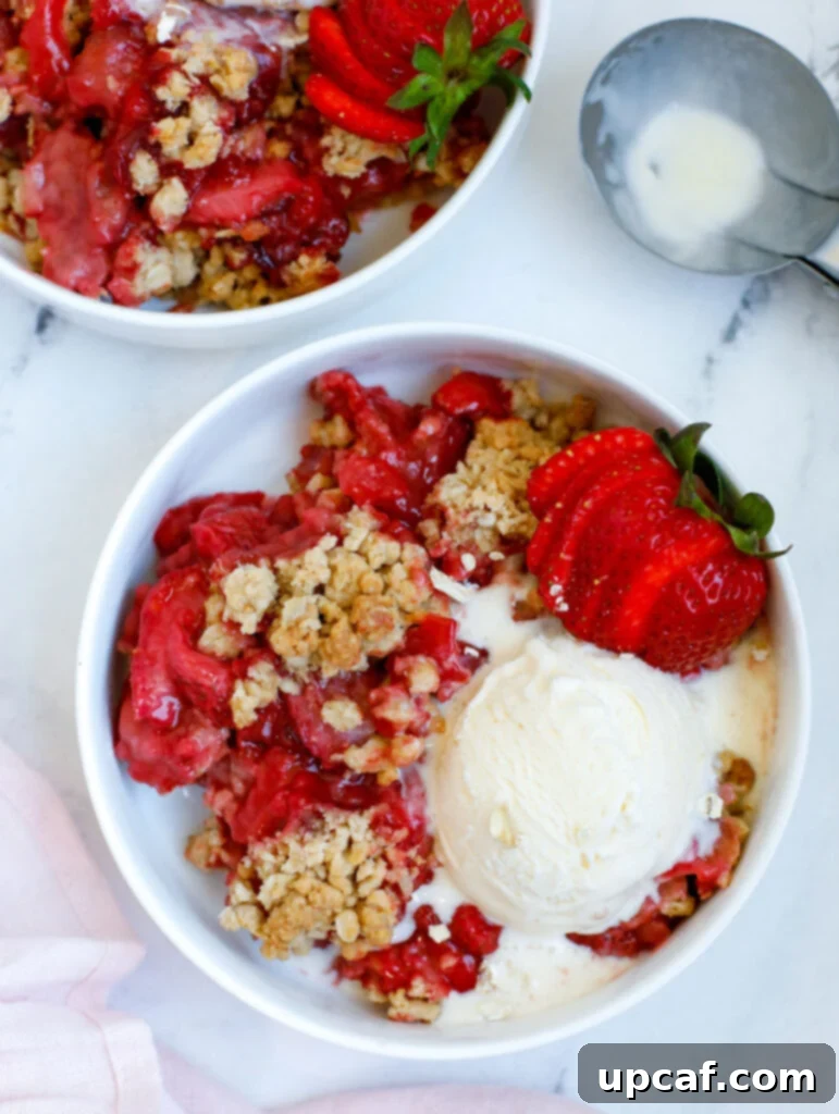 A bowl of warm Strawberry Crisp topped with a scoop of melting vanilla ice cream, ready to be enjoyed.