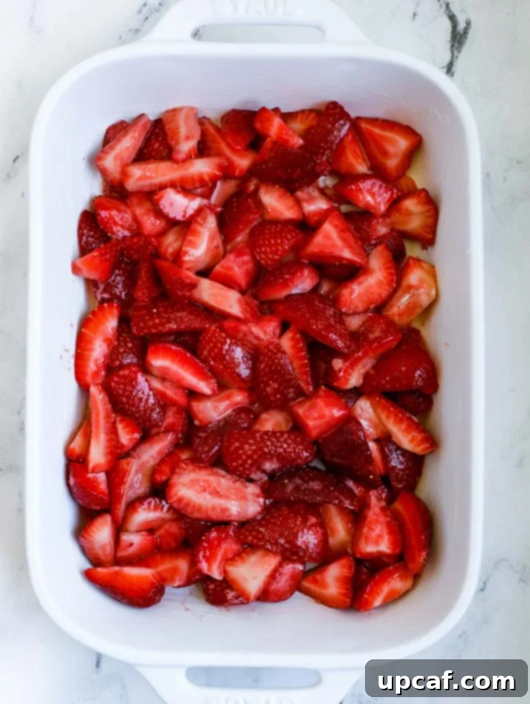 Fresh strawberry filling evenly spread in a buttered baking dish, ready for the topping.