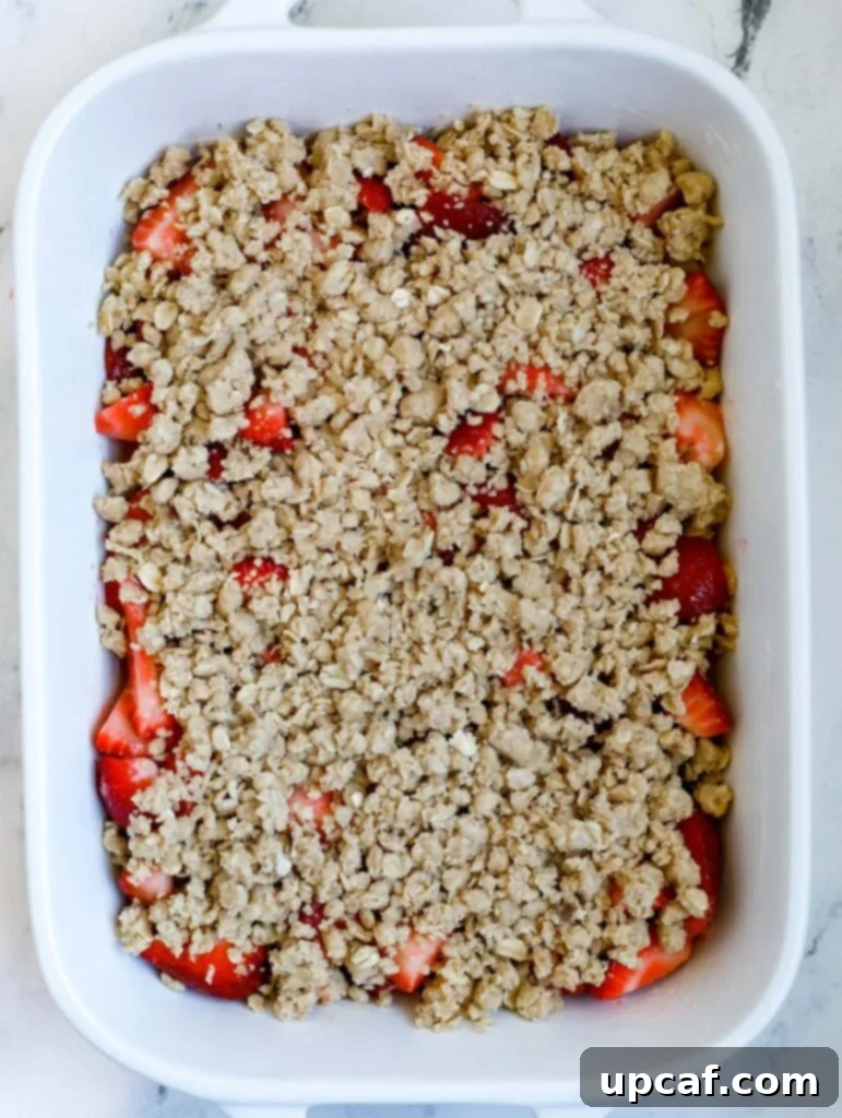 Unbaked strawberry crisp in a baking dish, with the crumb topping spread over the fruit, ready for the oven.