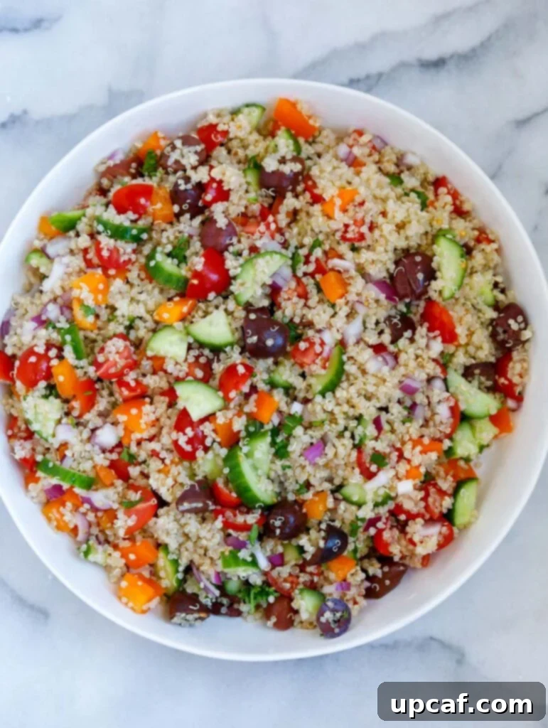 All the vibrant ingredients of the Mediterranean quinoa salad, including cooked quinoa, chopped vegetables, and olives, mixed together in a large bowl before adding the dressing.