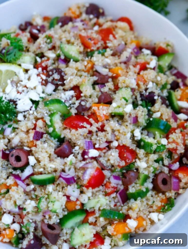 Close-up shot of the Mediterranean quinoa salad, highlighting the vibrant colors and textures of the quinoa, vegetables, feta, and olives, glistening with dressing.