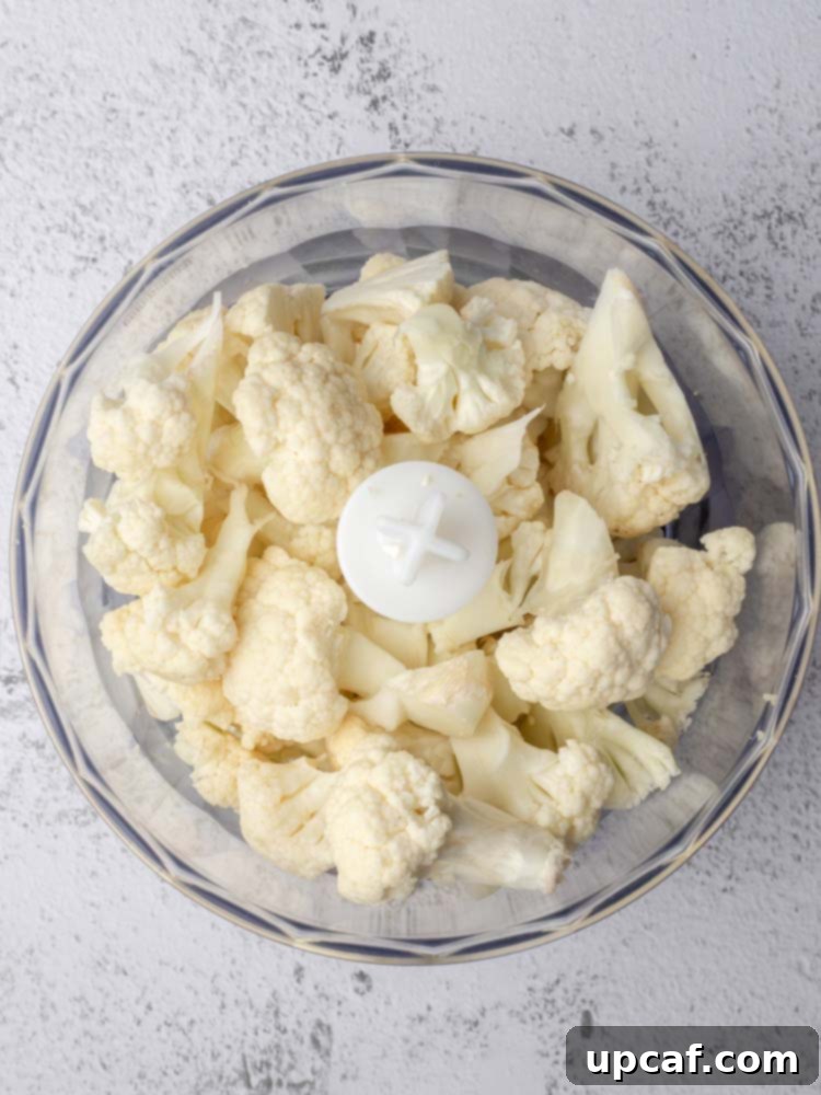 Cauliflower florets placed inside a food processor bowl, ready for ricing.