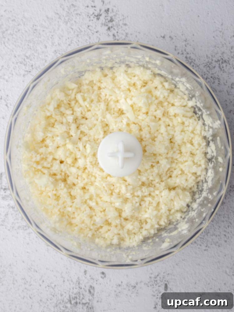 Finely riced cauliflower in a food processor, showing the ideal consistency after pulsing.