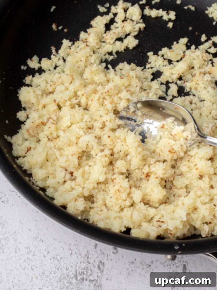 Cauliflower rice being sautéed in a skillet with olive oil, showing the cooking process.