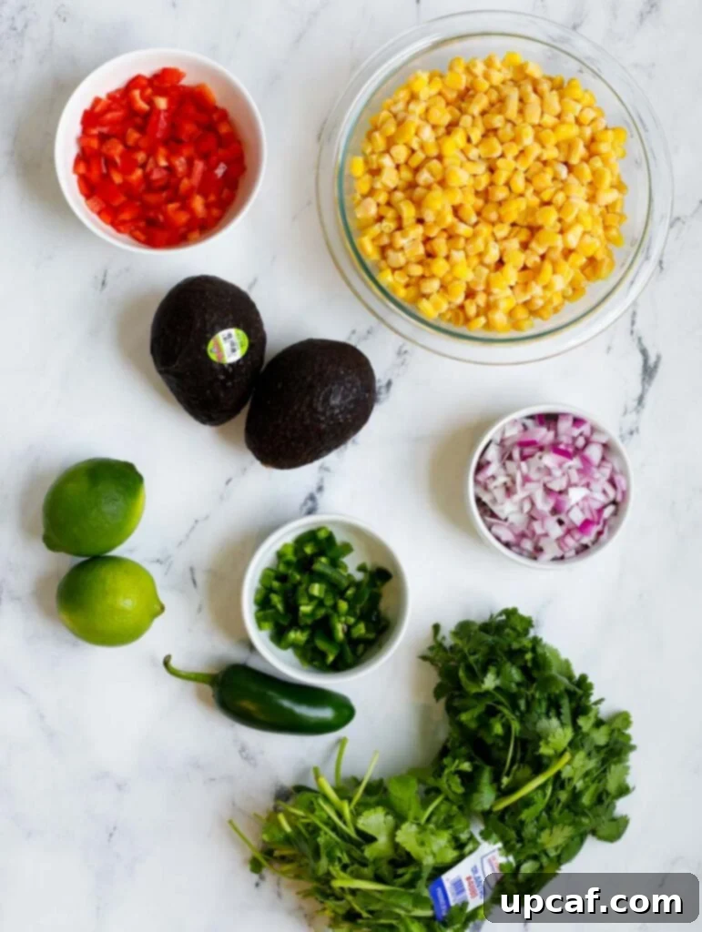 Ingredients for Mexican Street Corn Salad laid out on a white surface, including corn, bell peppers, avocados, onion, jalapeno, cilantro, and lime.