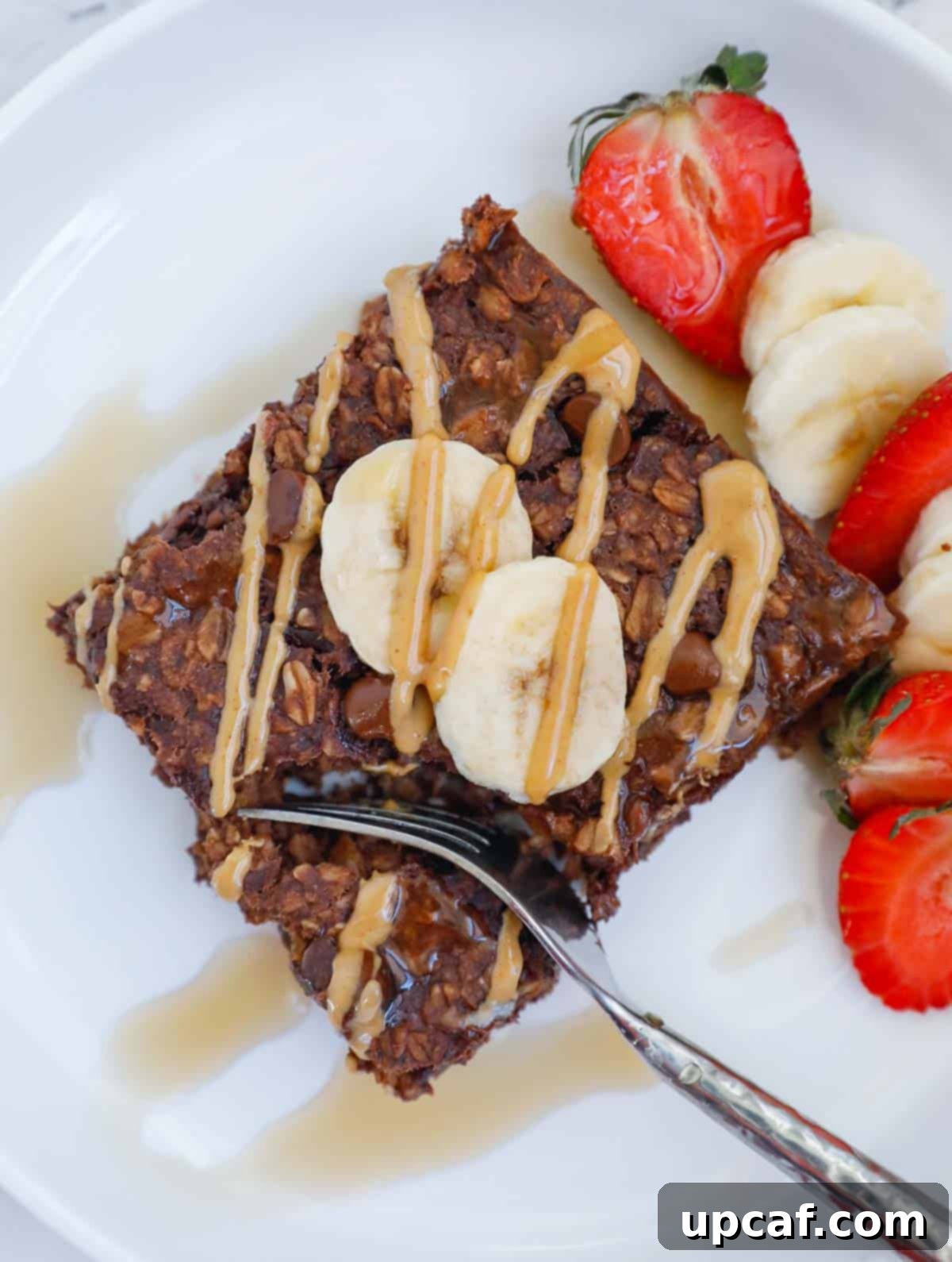portion of a square baked oat topped with peanut butter, banana and strawberry