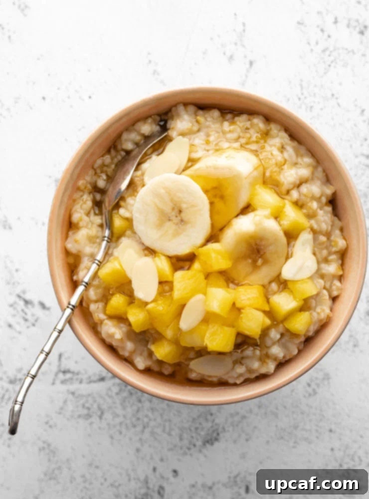 cooked oatmeal in a bowl topped with some pineapple, banana and honey