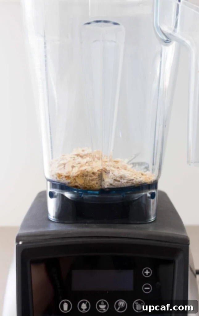 Rolled oats being poured into a blender, ready for blending into oat milk.