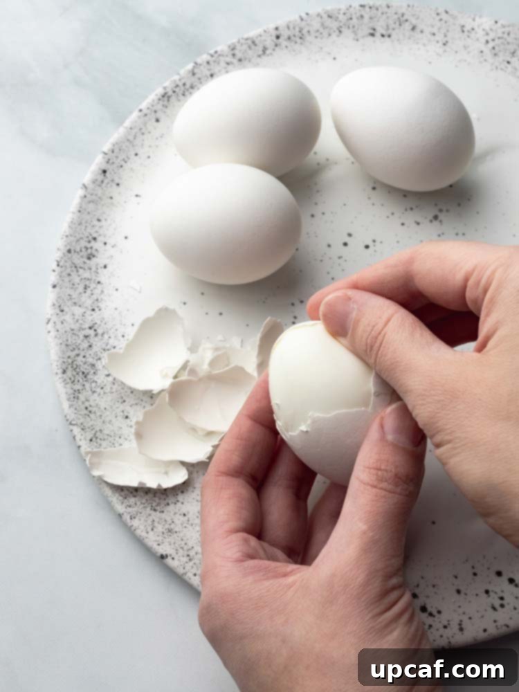 A hand gently peeling the shell off a hard-boiled egg, revealing the smooth white.