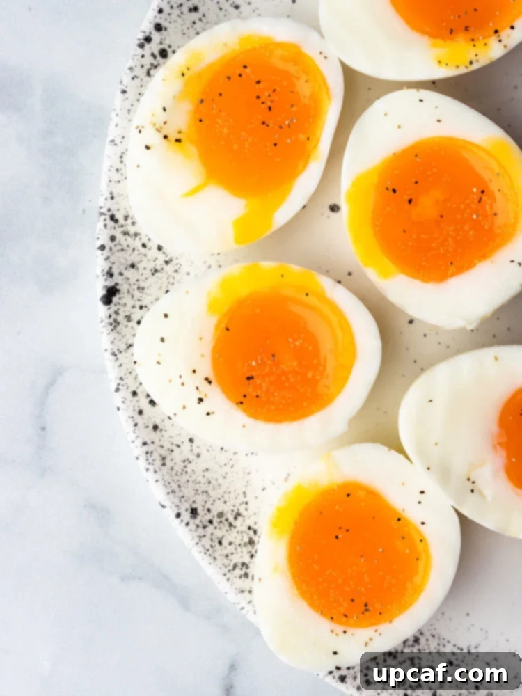 Two perfect soft boiled eggs, sliced in half, revealing their vibrant orange, creamy, and runny yolks, ready to be enjoyed as a topping for any meal.