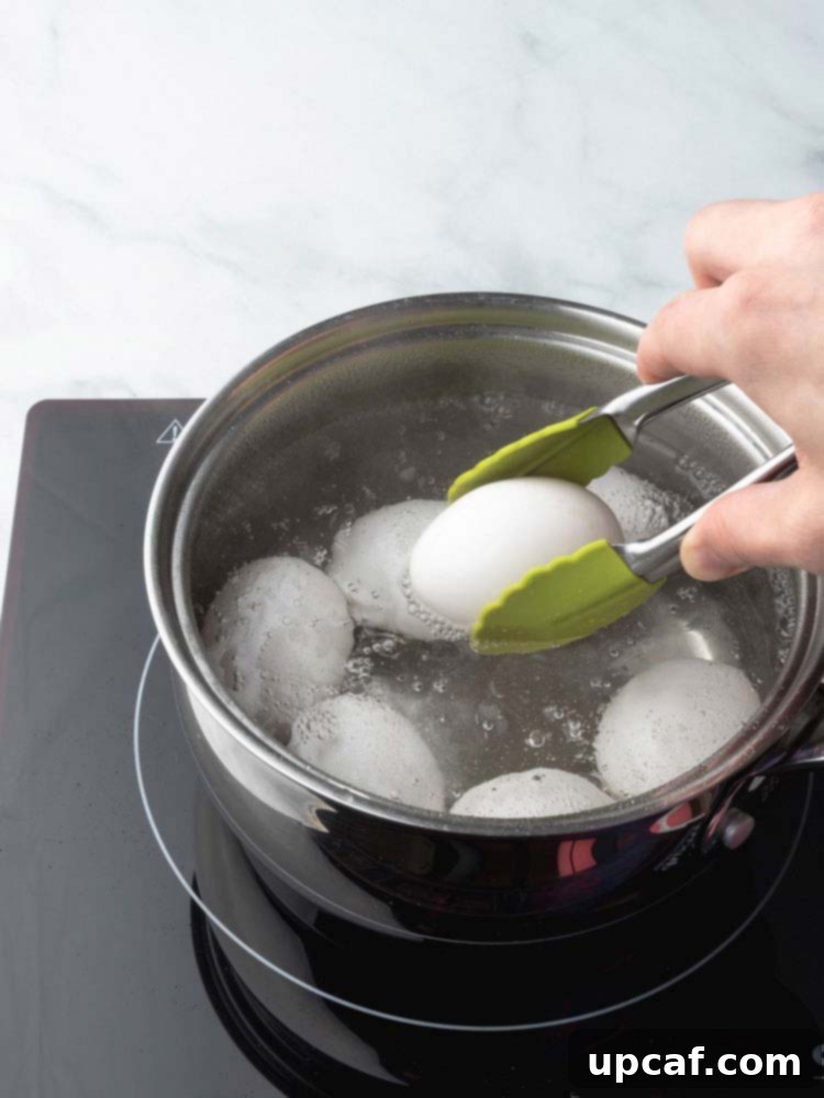 A kitchen tong carefully lowering a single egg into the simmering water, highlighting the gentle handling required to avoid shell damage.