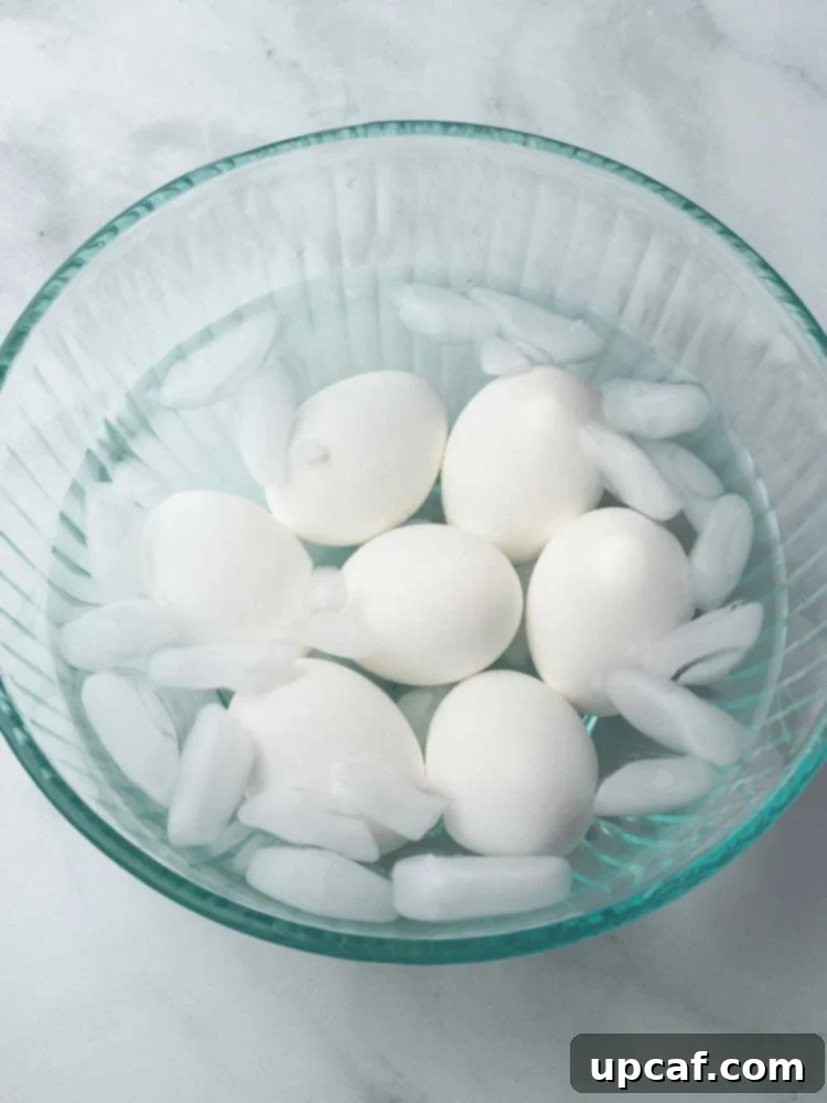 Cooked soft-boiled eggs immediately submerged in a bowl of ice water, crucial for stopping the cooking process and aiding in effortless peeling.