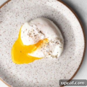 Poached egg on a plate, yolk cut through and seasoned with black pepper