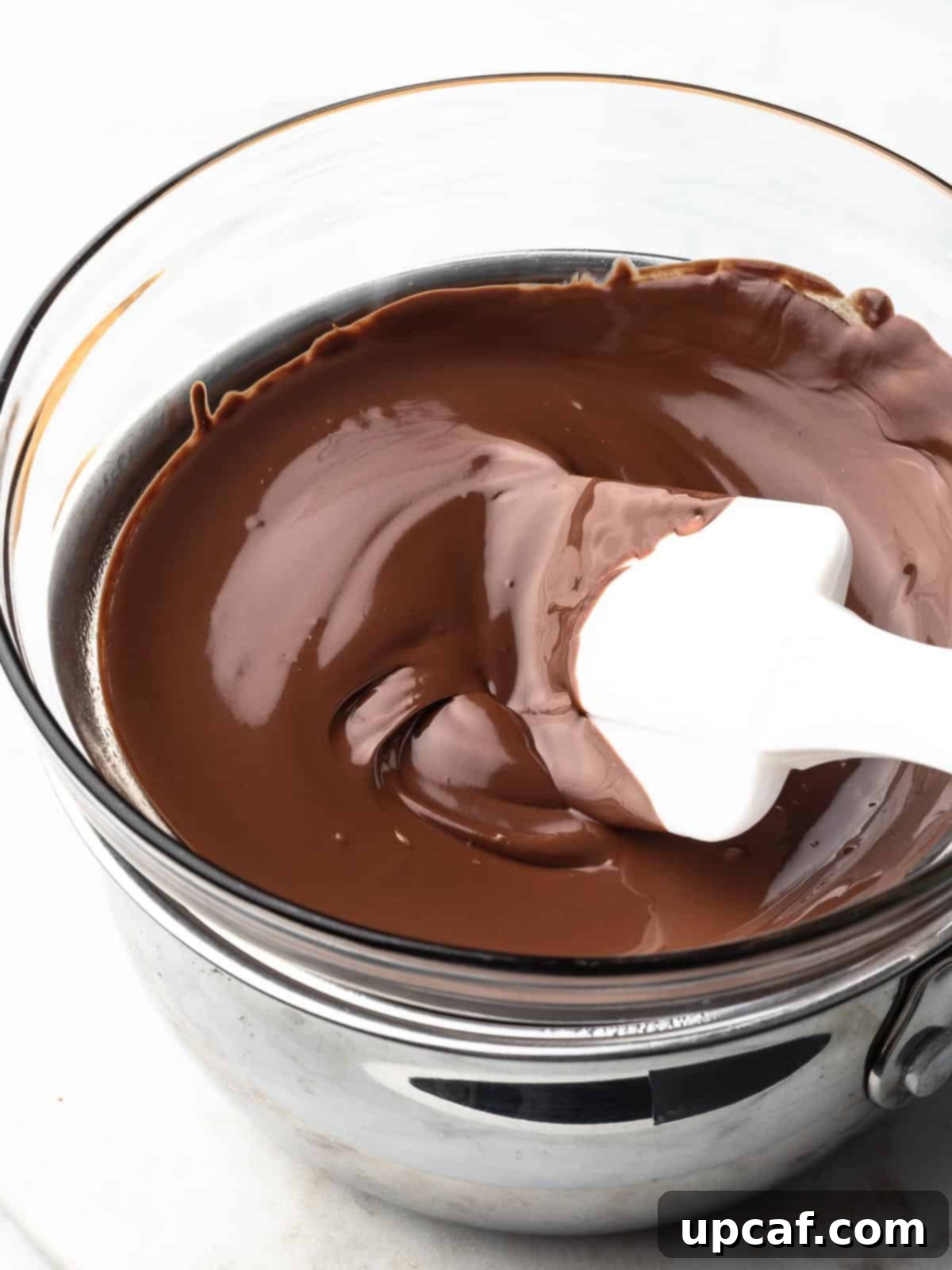 Smooth, melted chocolate in a double boiler with a spatula, indicating readiness.