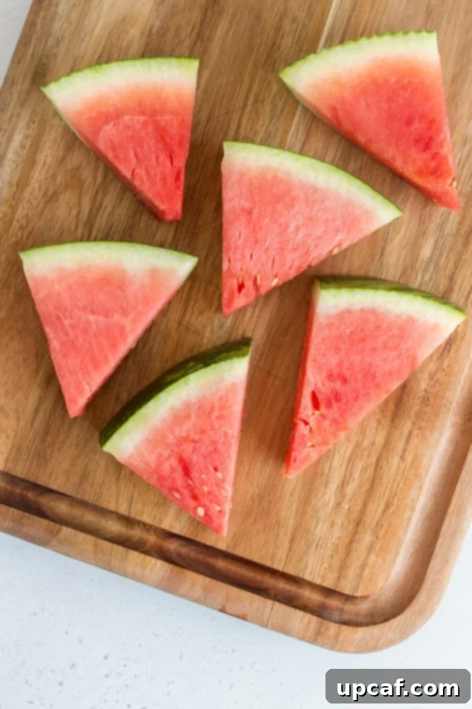 An overhead shot of fresh watermelon cubes and slices in a bowl, with a small portion of a whole watermelon in the background.