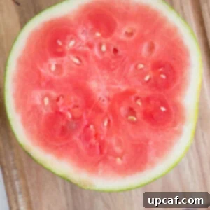 A watermelon cut cleanly in half, showcasing its vibrant red flesh, ready for further cutting.